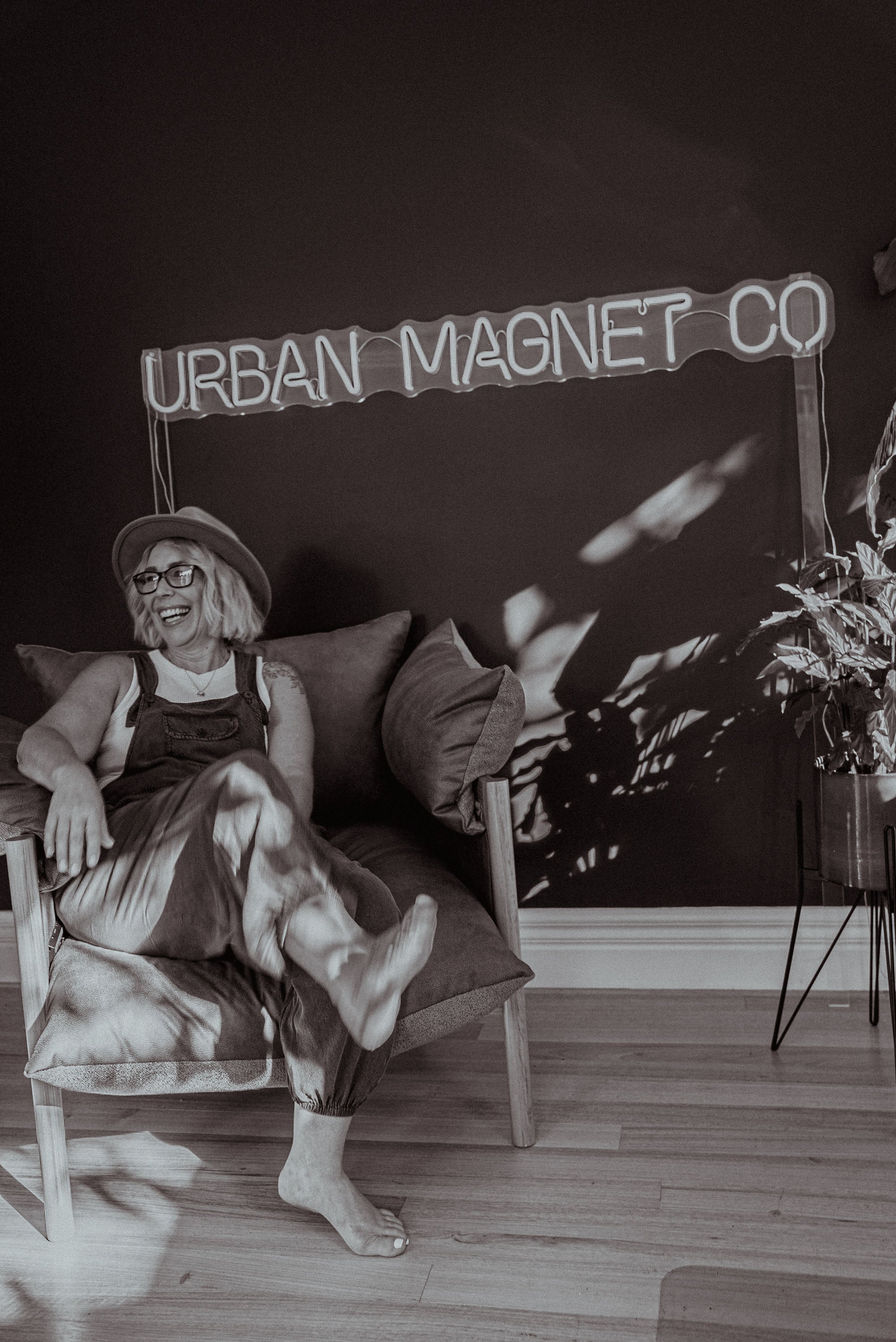 A photo of Urban Magnet Co Founder, Mel, sitting in a chair in front of a neon light that says Urban Magnet Co.