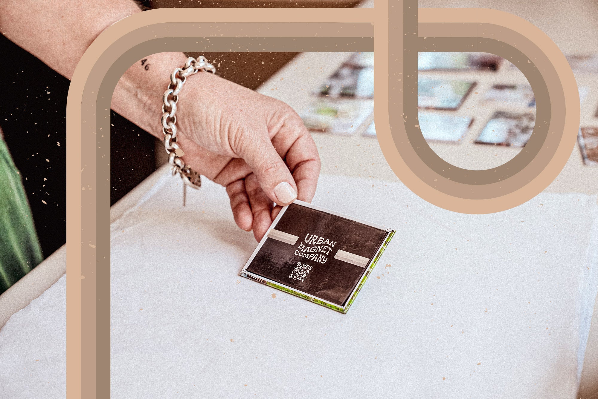 A hand with a silver bracelet holding a custom magnet with Urban Magnet Co's logo printed on it.