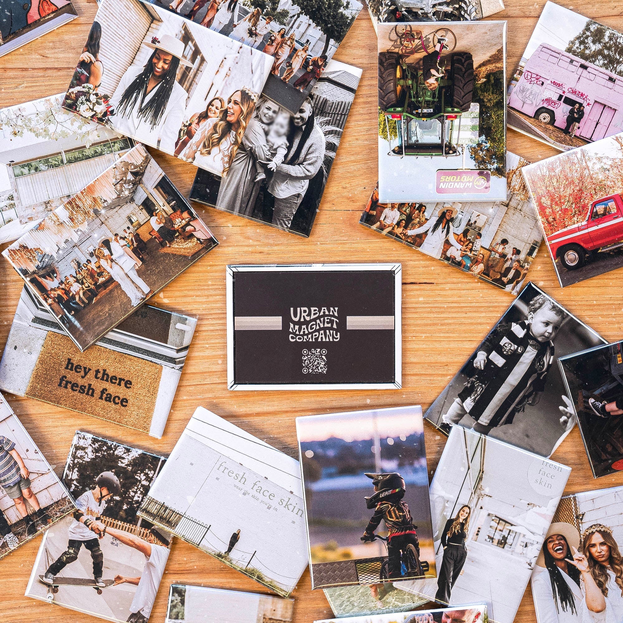 Lots of magnets spread out over a wooden table, all printed with different photos. There is a magnet with the Urban Magnet Co logo in the middle.