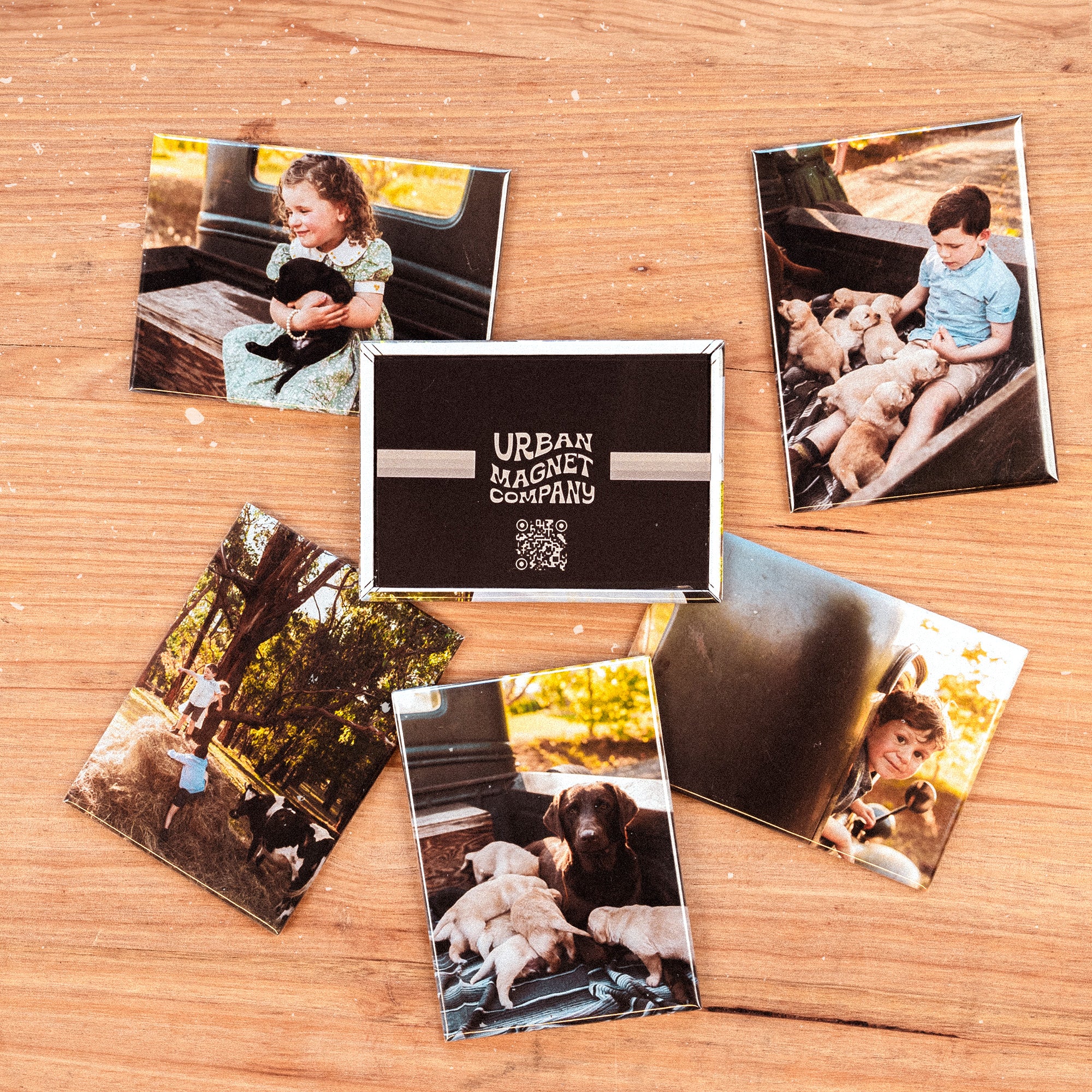 Five magnets printed with photos of children and puppies, and one magnet printed with the Urban Magnet Co logo, all displayed on a wooden table. 