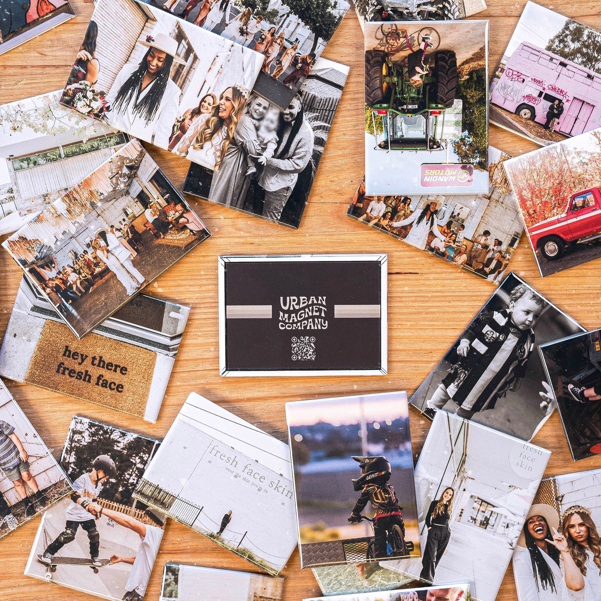 Lots of magnets spread out over a wooden table, all printed with different photos. There is a magnet with the Urban Magnet Co logo in the middle. 